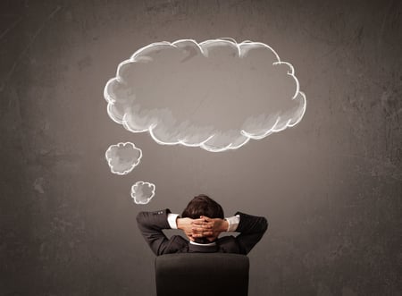 Young businessman sitting in office chair in front of a wall with cloud thought sketched on a chalkboard above his head